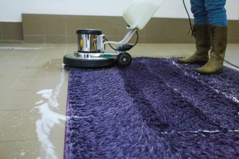 A person operates a vacuum cleaner on a purple rug, showcasing a professional carpet cleaning service in action.