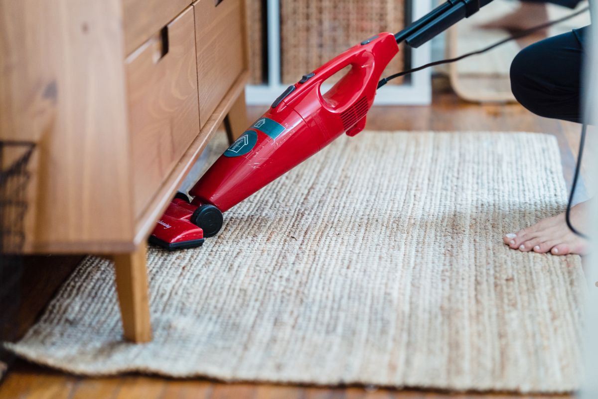 A person operates a red vacuum cleaner on a rug, effectively cleaning the carpet.