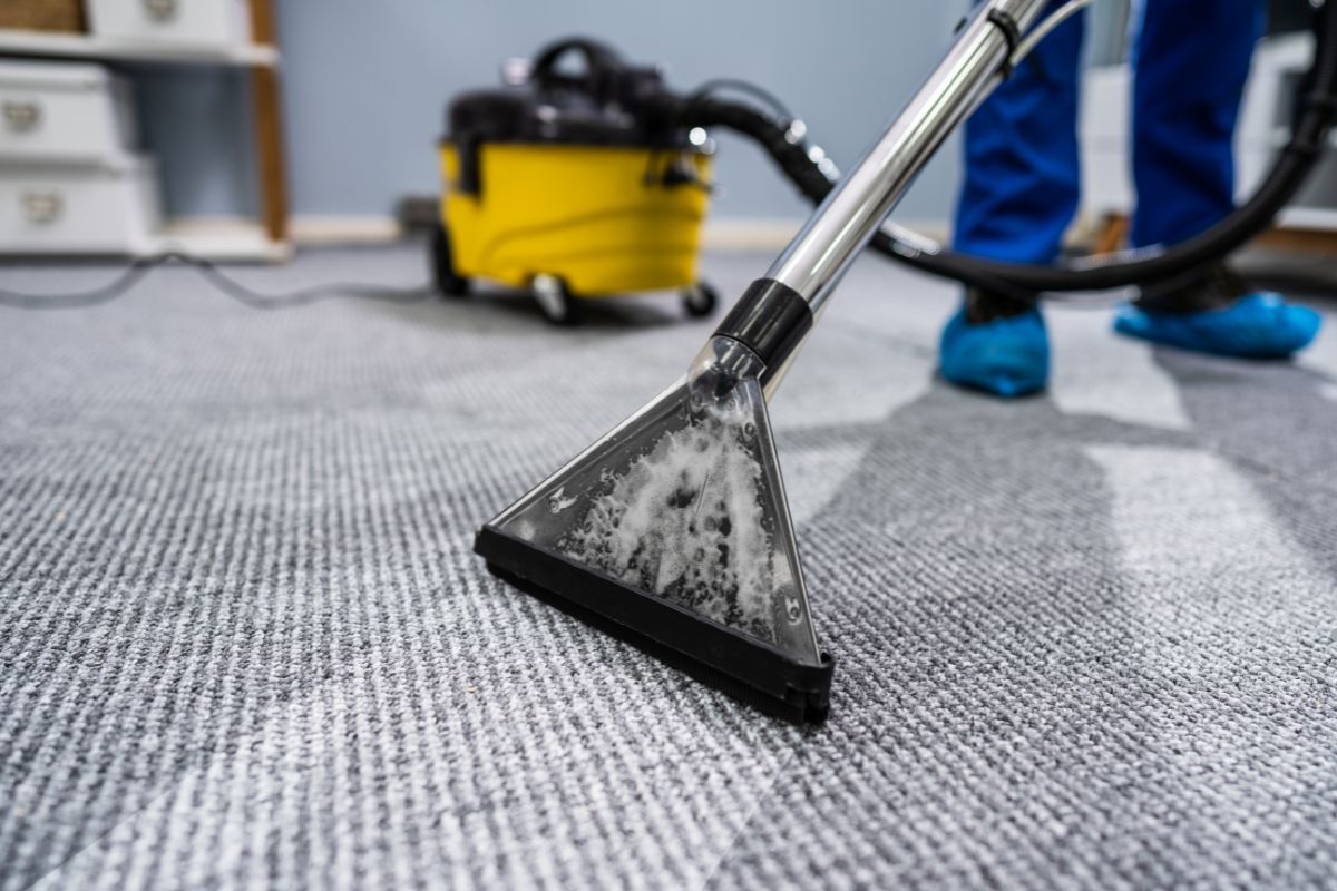 A person using a vacuum cleaner to clean a carpet in a well-lit room, focusing on removing dirt and debris.