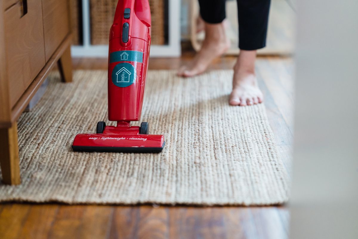 A person operates a red vacuum cleaner on a patterned rug, focusing on cleaning the surface effectively.