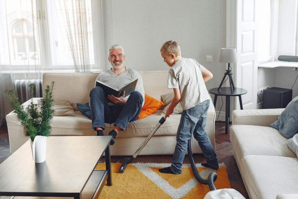 A man and a boy are tidying up a living room, organizing furniture and cleaning surfaces together.