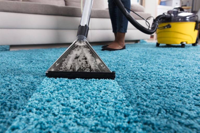 A woman vacuuming a blue carpet with a vacuum cleaner, focusing on cleaning the surface effectively.
